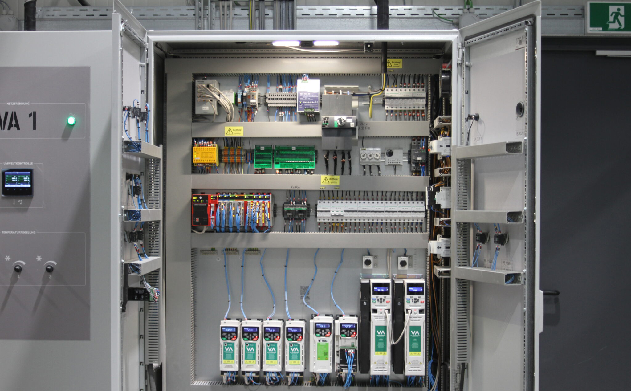 Elektroniker_2048x1365 – Feinguss Lobenstein Ein geöffneter Schaltschrank zeigt zahlreiche elektronische Komponenten, Kabel und Steuergeräte in strukturierter Anordnung. Die Anlage dient zur Steuerung und Überwachung technischer Prozesse.